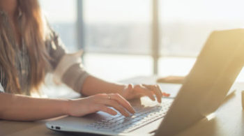 Female writer typing using laptop keyboard at her workplace in the morning. Woman writing blogs online, side view close-up picture