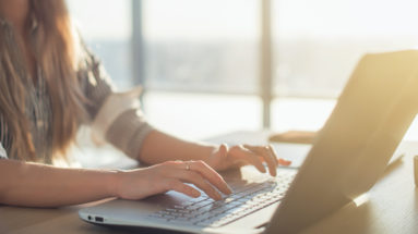 Female writer typing using laptop keyboard at her workplace in the morning. Woman writing blogs online, side view close-up picture